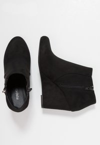 Para czarnych zamszowych botków na koturnie z bocznym zamkiem błyskawicznym, pokazanych z górnego i bocznego kąta na białym tle.