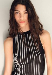Top senza maniche nero con righe verticali bianche, texture a coste e collo alto, caratterizzato da una vestibilità comoda e un design minimalista.