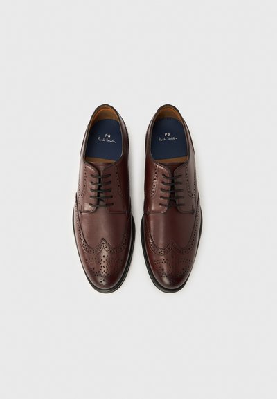 Viininpunaiset nahkaiset juhlakengät brogue-yksityiskohdilla, nauhakiinnitys, sileä tekstuuri ja musta kumipohja. Sisäpuolella on merkitty sisäpohja.