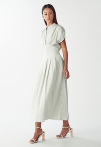 Pruhované midi šaty v světlé zelené a bílé barvě, s přiléhavým korzetem, balónovými rukávy a skládání sukní. Doplněné sandály na tenkých podpatcích.