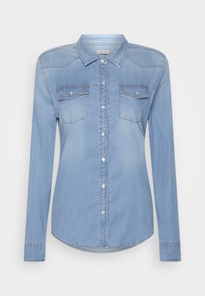 Chemise en denim bleu clair à manches longues, fermeture boutonnée sur le devant, col pointu et deux poches poitrine avec rabats boutonnés.
