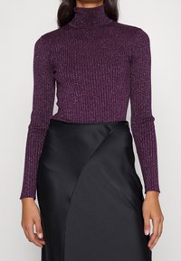 Fialový žebrovaný rolák s leskem, s dlouhými rukávy. Doplněný černou saténovou sukní s převazovaným designem.