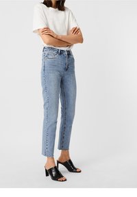 Ljust blå högmidjade jeans med rak passform, fransad nederkant och klassisk femfickdesign, i kombination med svarta sandaler med öppen tå och blockklack.