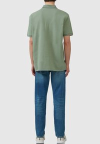 Polo de algodón verde con cuello clásico, manga corta y acentos de canalé a juego, combinado con jeans de mezclilla de lavado medio.