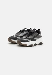 Black and grey sneakers with mesh and leather upper, thick white midsole, contrasting rubber outsole, and decorative stitching details.