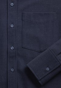 Camicia blu navy con bottoni, realizzata in tessuto strutturato, maniche lunghe con polsini con bottoni e tasca sul petto per praticità.