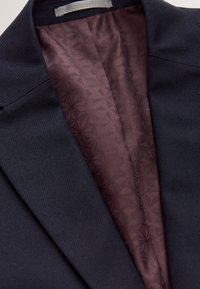 Mereväravi ülikonnajakk tekstureeritud välispinnaga. Sisemine vooder on sügavbordoopunase geomeetrilise mustriga. Märkimisväärne kahekordne õmblusdetail.