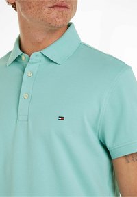 Polo shirt azzurro chiaro in tessuto texturizzato, con colletto classico e tre bottoni, e un piccolo logo sul lato sinistro.