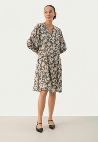 Blumenkleid mit Puffärmeln, V-Ausschnitt, in neutralen Farbtönen. Leichter Stoff, lockere Passform und knielanger Saum. Schwarz-weißes Muster.