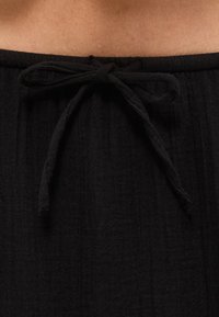 Μαύρη ριγωτή ζώνη παντελονιού με δεμένο κορδόνι κάτω από γυμνό δέρμα στη μέση.