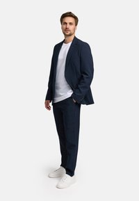 Giacca da abito blu navy sopra una t-shirt bianca, abbinata a pantaloni navy e sneakers bianche. Linee pulite e vestibilità moderna.