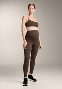 Ruskea urheiluliivit ja korkeavyötäröiset legginsit, sileä rakenne, joustava kangas, yhdistetty mustiin urheilukenkiin. Yksinkertainen, moderni muotoilu.