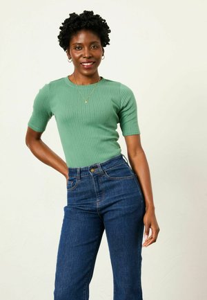 Green ribbed knit shirt with short sleeves, paired with high-waisted blue denim jeans featuring a button closure and front pockets.