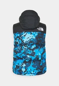 Vesta s prošíváním s černou kapucí a modrým maskáčovým vzorem. Má lesklou, prošívanou texturu a logo North Face na rameni.