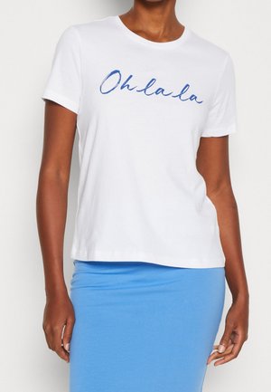 Person wearing a white short-sleeve T-shirt with “Oh la la” in blue script and a light blue skirt, standing against a plain background.