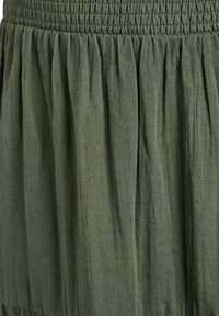 Jupe en mélange de coton vert olive, avec une taille smockée et un tissu doux et texturé avec des plis froncés pour un design fluide.