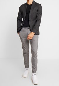 Blazer gris à rayures sur une chemise noire, associé à un pantalon gris ajusté et des baskets blanches, avec une coupe slim et un design épuré.