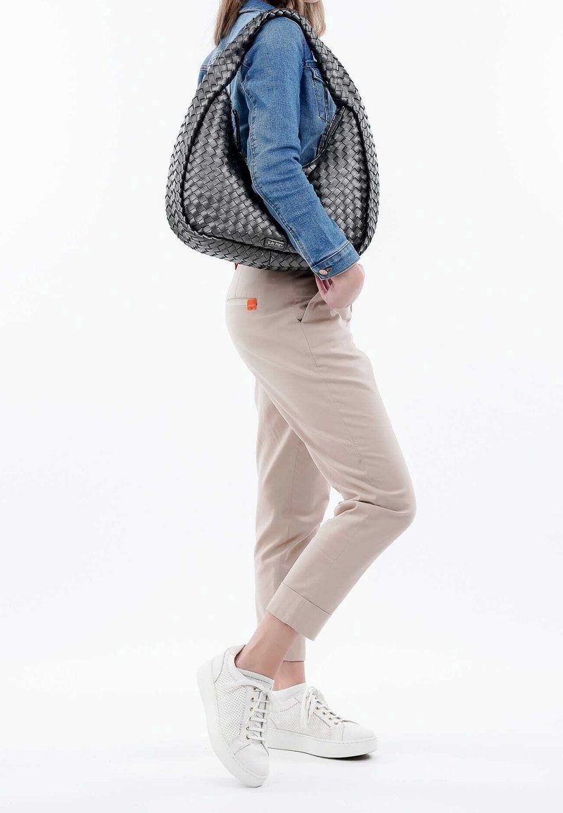 Sac hobo en cuir tressé noir avec une finition texturée, accompagné d'une veste en denim et d'un pantalon beige, assorti à des baskets blanches.