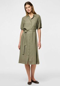 Abito camicia in lino verde oliva con design a bottoni, maniche corte e cintura in vita. Presenta una tasca sul petto e lunghezza a metà polpaccio.