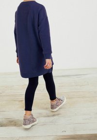 Námořnická mikinová šaty s dlouhými rukávy, doplněné černými legínami a kovově lesklými vysokými teniskami, pohled zezadu.