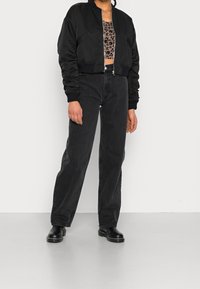 Mustat bomber-tyyliset takki, jossa on lyhyt leikkaus, ribbikuvioidut hihansuut ja etuvetoketju. Yhdistetty korkeavyötäröisiin mustiin farkkuihin ja mustiin nilkkureihin.