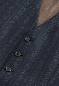 Marineblauwe suitstof met fijne verticale strepen, voorzien van vier donkere knopen en een gestructureerde, tan voering. Zachte, geweven stof.