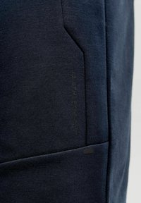 Tissu bleu marine foncé avec un gros plan sur une couture de poche et des détails subtils de texte vertical sur le côté.