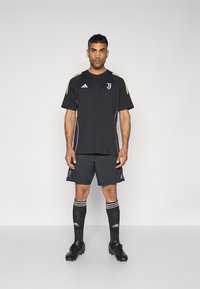 Maillot de sport noir avec des accents jaunes et bleu clair, associé à un short gris foncé, des chaussettes de sport noires et des crampons noirs, avec des rayures.