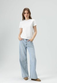 Wit T-shirt met korte mouwen gecombineerd met lichtblauwe denim jeans met wijde pijpen. De jeans heeft een hoge taille en steekzakken aan de voorkant. Bruine laarzen maken de outfit compleet.