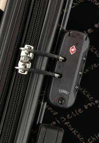Detail des Reißverschlusses eines schwarzen Koffers mit TSA-Schloss, Metallbeschlägen und strukturiertem Oberflächen. Verfügt über ein Zahlenkombinationsschloss und glatte, gerade Reißverschlüsse.