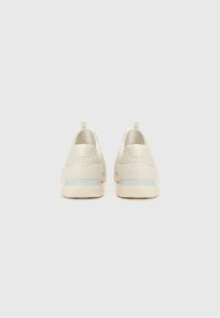 White textured sneakers with a smooth heel design, a light blue accent on the sole, and yellow pull tabs at the back.