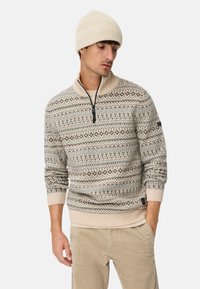 Beige strikket pullover med mønstrede designs i brune og grå nuancer, lynlåshals, ribbede manchetter, kombineret med en matchende cremefarvet beanie.