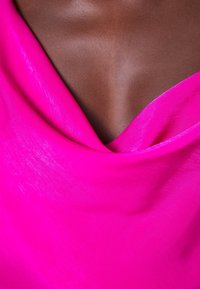 Primo piano di un petto di pelle scura avvolto in un drappo di tessuto setoso rosa brillante con scollatura a cappuccio.