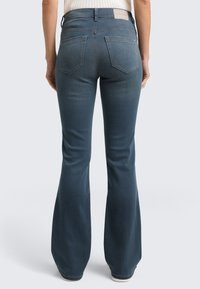 Dunkelblaue, ausgestellte Jeans mit mittelhohem Bund, ausgestattet mit zwei Gesäßtaschen und einem markierten Lederpatch am Bund. Weiche Denim-Textur.