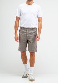 Lichtgrijze shorts met een elastische tailleband, een sluiting met een voorsluiting, en zijzakken. Gecombineerd met een effen wit T-shirt en klassieke sneakers.