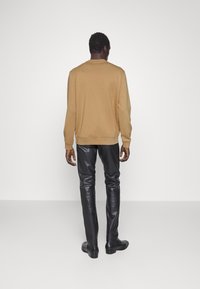 Suéter de punto color bronce, vista trasera, combinado con pantalones ajustados de cuero negro y zapatos negros. Textura suave con puños y dobladillo acanalados.