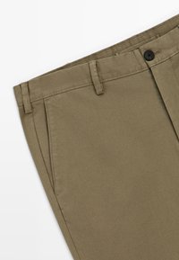 Khaki-Chinos mit glatter Textur, geradem Schnitt, Seitentaschen und einem einzelnen schwarzen Knopfverschluss am Bund.