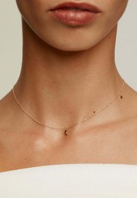 Collar de cadena de oro con un pequeño colgante en forma de luna creciente, diseño delicado, enlaces finos y un acabado suave contra la piel desnuda.