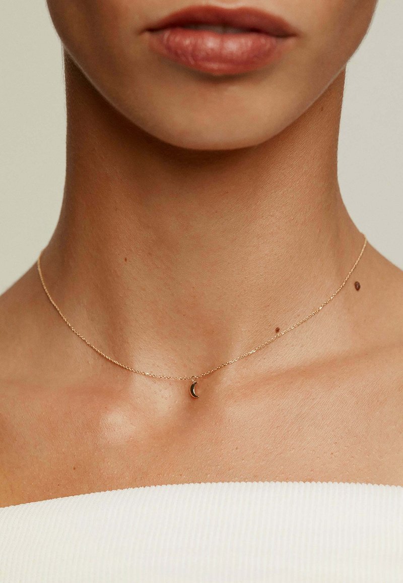 Collar de cadena de oro con un pequeño colgante en forma de luna creciente, diseño delicado, enlaces finos y un acabado suave contra la piel desnuda.