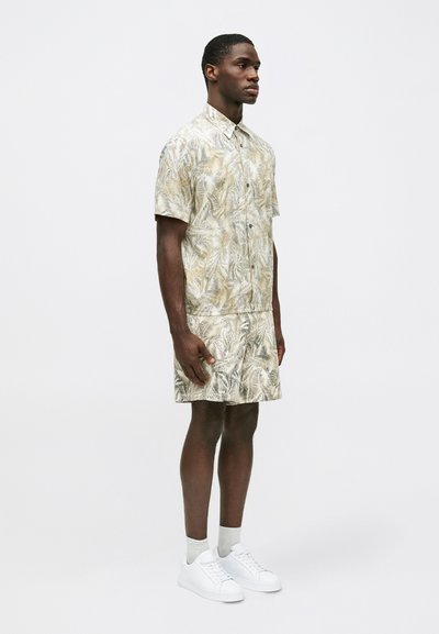 Chemise à manches courtes avec boutons et short assorti en beige clair, imprimé de feuilles de palmier. Dotée d'un col classique et d'une coupe décontractée. Baskets blanches.