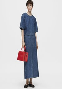 Conjunto de dos piezas de denim que incluye una blusa de corte cuadrado y una falda maxi. El conjunto se complementa con un bolso de cuero rojo con logo en relieve y zapatos negros.