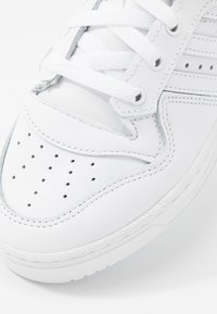 Sneaker in pelle bianca con dettagli perforati, lacci piatti e suola testurizzata. Presenta cuciture sottili e un design della punta arrotondata.