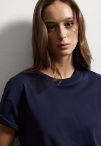 T-shirt blu navy con scollatura rotonda e maniche corte arrotolate, realizzata in tessuto morbido, caratterizzata da una superficie liscia e senza motivi visibili.