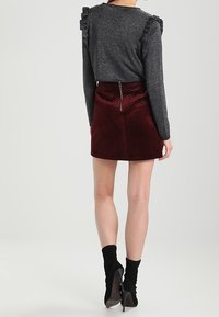 Svart, glittrig långärmad topp med volanger på axlarna, parat med en burgundyröd mini kjol i zigzag-mönster, med dragkedja bak. Strumpor är svarta.