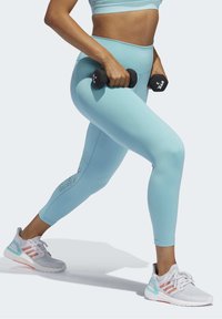 Leggings da allenamento blu chiaro con vita alta e dettagli in rete testurizzata. Abbinate a scarpe da ginnastica grigie e rosa, mentre si tengono manubri neri.