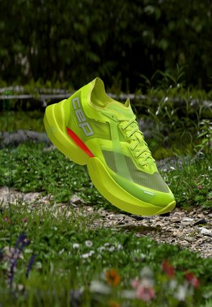Neon yellow running shoe with red heel detail and "CEP" logo floats above a grassy, rocky outdoor path with blurred greenery background.
