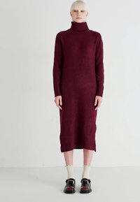 Burgundy knit turtleneck dress with long sleeves, mid-calf length, and ribbed accents at the hem, paired with black shoes and white socks.