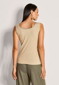 Beige geripptes Tanktop mit einem runden Ausschnitt und silbernem Rand. Der Stoff wirkt glatt, körpernah geschnitten, ohne zusätzliche Muster oder Akzente.
