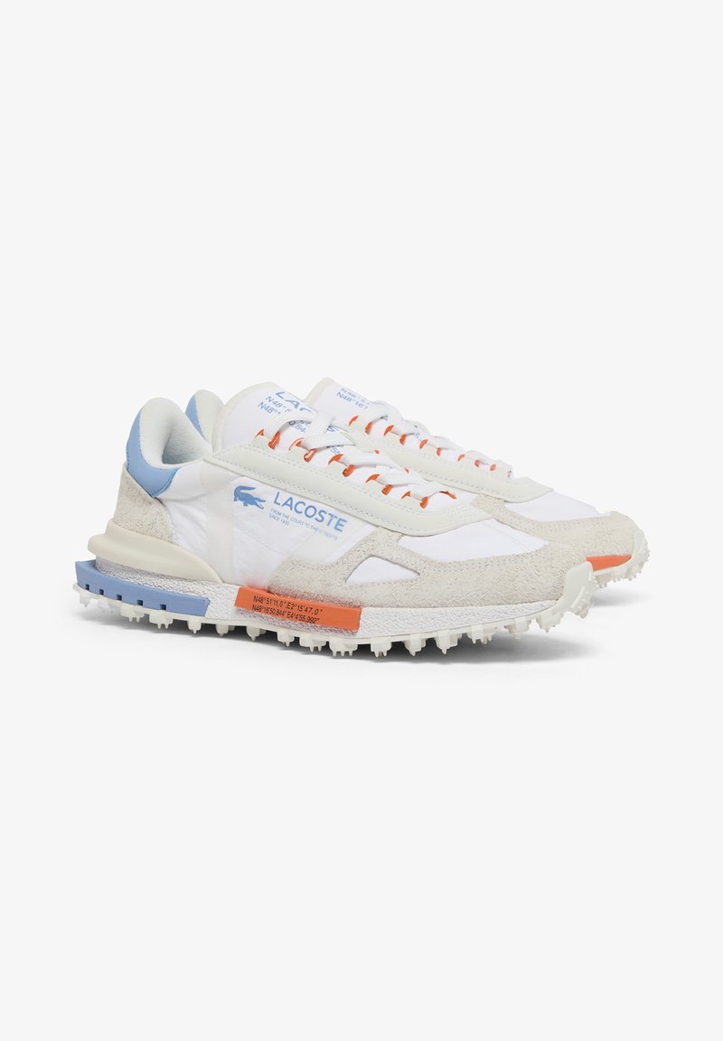 White and beige Lacoste sneakers with blue and orange accents, textured sole, visible logo, and lace-up design on a white background.