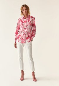 Blomstrede skjorter med pink og hvide mønstre, parret med hvide tapered bukser og pink strophæle. Glat stoftekstur.